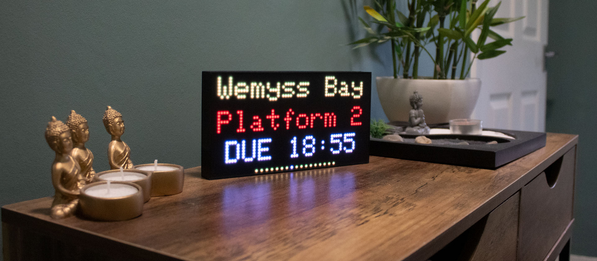 A WeePixelBox showing live train information on a wooden sideboard